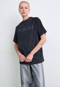 Zwarte T-shirt met korte mouwen en een gestructureerde afwerking, met een glanzend "TEAMGEIST" logo. Draagt met lichtzijden zilveren broek.