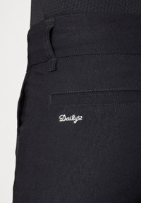 Pantaloni neri con una texture liscia, una tasca laterale e un logo ricamato "Daily" in argento sulla tasca posteriore.