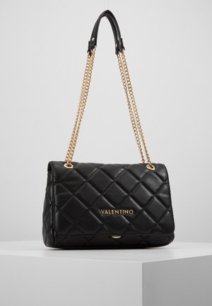 Bolso de piel acolchado negro con cadenas doradas y una placa con el logo. Presenta un diseño de solapa y una textura suave, adecuado para uso formal.