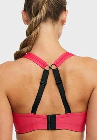 Roze sportbeha met verstelbare zwarte bandjes, voorzien van een haaksluiting en een gladde textuur. Het ontwerp heeft een racerback-stijl.