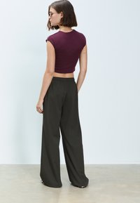 Donkerrood cropped shirt met korte mouwen, gecombineerd met loszittende, donkergroene broek. Gladde textuur en elastische tailleband bij de broek.