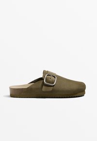 Olivgrön mocka slip-on sandal med en fyrkantig silverfäste och ljusbrun korksula. Har en konturerad, texturerad fotbädd och gummisula.