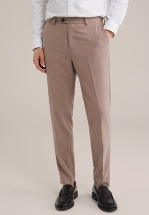 Pantalones beige a medida con un acabado texturizado, pliegue delantero único y cierre de botón clásico. Llevados con mocasines de cuero negros.