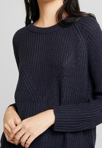 Ciemnoniebieski sweter z dzianiny o fakturowanym wzorze. Posiada okrągły dekolt oraz długie, żebrowane rękawy, prezentując luźny krój.