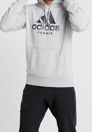 Sweat à capuche Adidas gris avec un logo graphique noir portant les mots "adidas" et "TENNIS". Comprend une poche frontale et un cordon de serrage ajustable.