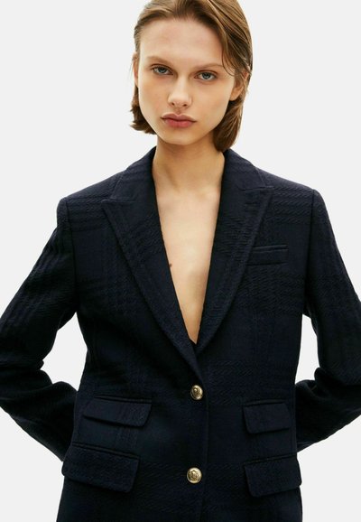 Marineblauer Blazer mit strukturiertem Finish, featuring einem tiefen V-Ausschnitt, goldenen Knopfverschlüssen und zwei aufgesetzten Taschen vorne.