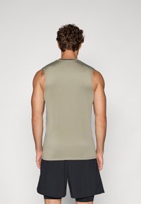 Ujjatlan sportfelső világos olajzöld színben, sima tapintással. Kerek nyakkivágással és a hátsó oldalán nyomtatott "NIKE PRO" logóval rendelkezik.