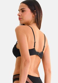 Soutien-gorge en dentelle noire avec des bretelles fines réglables et un fermoir à crochets au dos. Tissu texturé avec des accents délicats.