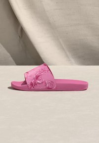 Șlapi roz cu design floral pe bretea, realizați din material flexibil. Dispune de talpă interioară texturată și talpă plată.