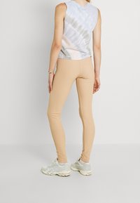 Vaaleansininen ja kerma-häivytetty hihaton paita, jonka parina tiukat beige leggingsit ja vaaleanharmaat urheilujalkineet, nähtynä takaa.