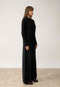 Czarny sweter z prążkowanego dzianiny z okrągłym dekoltem w połączeniu z szerokimi, ciemnozielonymi spodniami z korduroy. Całość dopełniają brązowe buty na platformie.