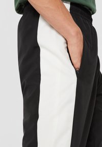 Svarta träningsbyxor med en vit sidopanel. Tillverkade av ett mjukt, lätt material med en ficka med dragkedja på sidan.