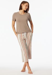 T-shirt beige a maniche corte abbinato a pantaloni a righe, lunghi fino al ginocchio, con linee arancioni, verdi e beige, realizzati in tessuto leggero.