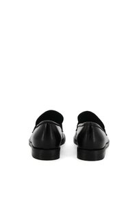 Scarpe slip-on in pelle nera con texture liscia, punta arrotondata e colletto imbottito. Sole piatto, dettaglio di cucitura sottile, design minimalista.