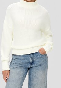 Biały sweter dziany z wysokim kołnierzem, luźnym krojem i ściągaczami, w połączeniu z jasnoniebieskimi podartymi jeansami.