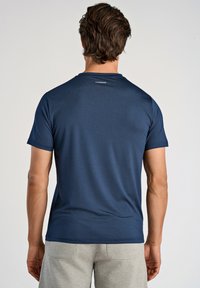 Marineblå kortærmet T-shirt med struktureret stof, rund udskæring og et lille mærke bagpå. Bæres med grå shorts.