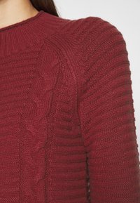 Pull bordeau à côtes avec détail en maille torsadée sur l'épaule, doté d'un col ras du cou et d'un tissu texturé.