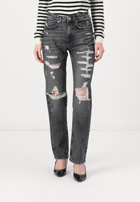 Distressed black jeans with a straight-leg cut, featuring multiple rips, light fading, and a button closure. Paired with shiny black heels.