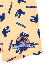 Costume da bagno giallo con un motivo di silhouette di dinosauri blu e la scritta "Jurassic World", con un logo iconico in basso a sinistra.