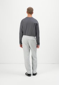 Camisa de manga larga gris, de corte relajado, combinada con pantalones de chándal ligeros grises con cintura elástica. El conjunto es simple y casual, sin patrones visibles.