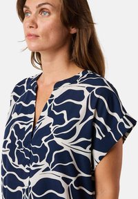 Marinebluse mit weißem abstraktem Blumenmuster, kurzen Ärmeln, V-Ausschnitt und weichem Stoff. Fluide Form mit bequemer Passform.