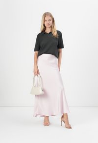 Camiseta polo preta de manga curta, saia maxi de cetim rosa-claro, sapatos de salto strappy bege e uma pequena bolsa branca. Texturas suaves e design fluido.