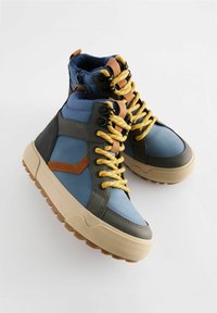 Hoge sneakers in blauw, grijs en bruin leer met gele veters, getextureerde rubberen zolen en contrasterende bruine accenten.