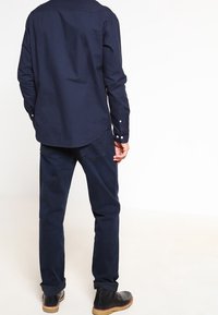 Mörkblå skjorta med knappar, rundad nederkant, långa ärmar och en mjuk textur, ihop med matchande mörka byxor och svarta ankelstövlar.