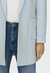 Blazer cu un model în zig-zag de culoare albastru deschis, cu un buzunar aplicat, purtat cu blugi de denim de culoare albastru închis. Blazerul are o închidere cu un singur nasture și revere cu vârf.