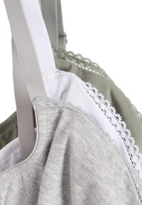 Trois soutiens-gorge en tissus gris, blanc et vert olive. Chacun présente des bretelles ajustables et des détails en dentelle le long des bords pour une texture supplémentaire.
