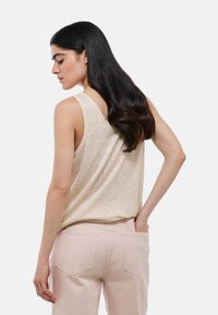 Top sans manches beige avec une coupe décontractée, fabriqué dans un tissu léger, associé à un pantalon taille haute rose clair avec deux poches arrière.