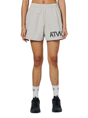 Person iført lysegrå træningsshorts med bogstaverne "ATW" på det ene ben, hvide mærkesokker og sorte løbesko, stående oprejst.