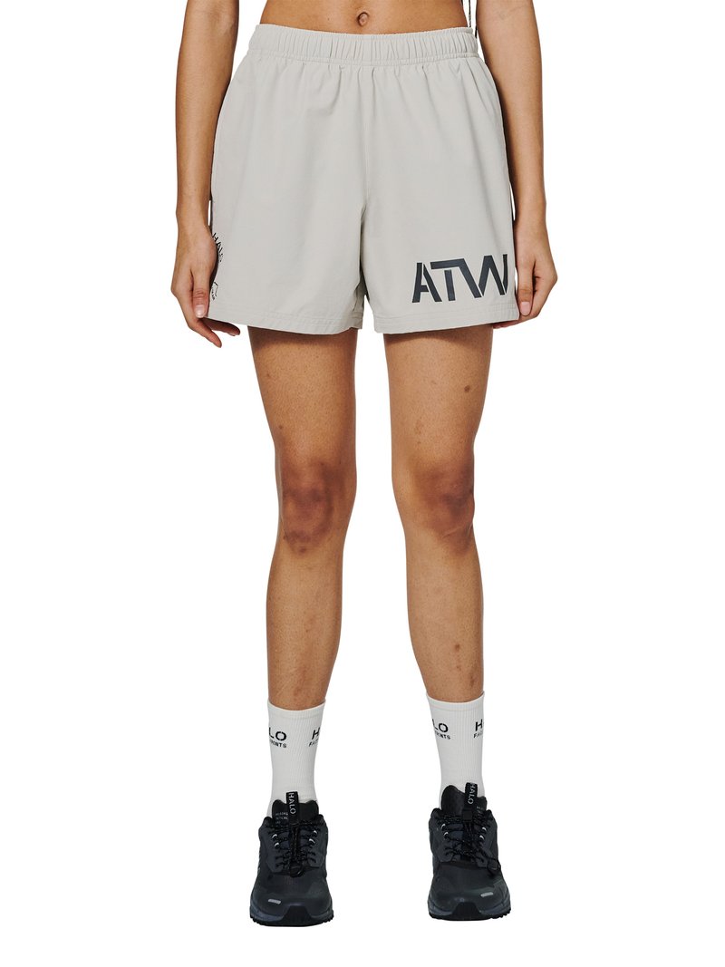 Person iført lysegrå træningsshorts med bogstaverne "ATW" på det ene ben, hvide mærkesokker og sorte løbesko, stående oprejst.