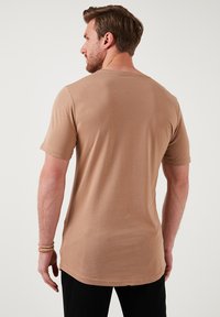 Hnědé tričko s krátkým rukávem vyrobené z hebkého materiálu, s kulatým výstřihem a mírně delší zadní částí pro pohodlné nošení.