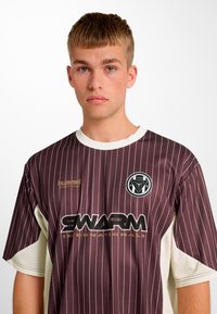 Brun og creme farvet stribet kortærmet jersey med rund halsudskæring, med et centralt logo og teksten "SWARM" i sort.