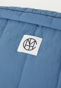 Tessuto imbottito blu con un design trapuntato, dotato di un'etichetta bianca prominente che mostra un logo circolare nero.