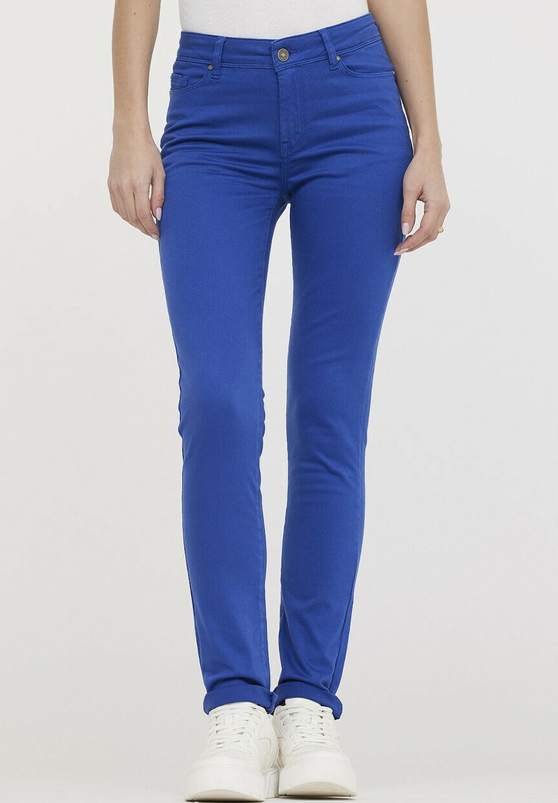 Jean skinny bleu en tissu extensible, avec une texture lisse, un design à cinq poches et une fermeture à bouton en métal à la taille.