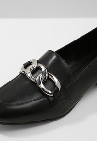 Czarny skórzany mokasyn z cienkim noskiem i dużym srebrnym łańcuchem z przodu.