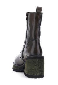 Bota de tobillo de cuero negro con un acabado texturizado, cierre de cremallera lateral y un tacón grueso de ante verde, que cuenta con una suela rugosa para mayor tracción.