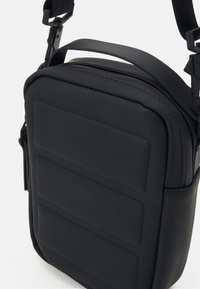 Schwarze Schultertasche mit glatter, gepolsterter Oberfläche, rechteckiger Form, verstellbarem Tragegurt und feinen Steppnähten.