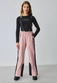 Juodas ilgomis rankovėmis viršus su "BAKER" logotipu, derinamas su šviesiai rožiniais kelnėmis, turinčiomis juodus šoninius panelius ir reguliuojamus dirželius, glotnios tekstūros.