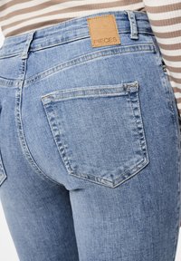 Blauwe denim jeans met een gestructureerde afwerking, voorzien van een vierkante patch met het label "PIECES" op de tailleband en twee achterzakken met stikseldetails.