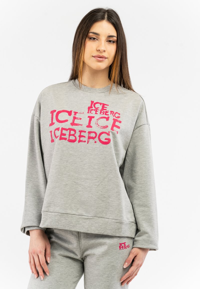 Grauer Sweatshirt mit verblasstem pinkfarbenem "ICEBERG"-Druck, lockerer Schnitt und gerippten Bündchen. Zusammen mit passenden grauen Hosen getragen.