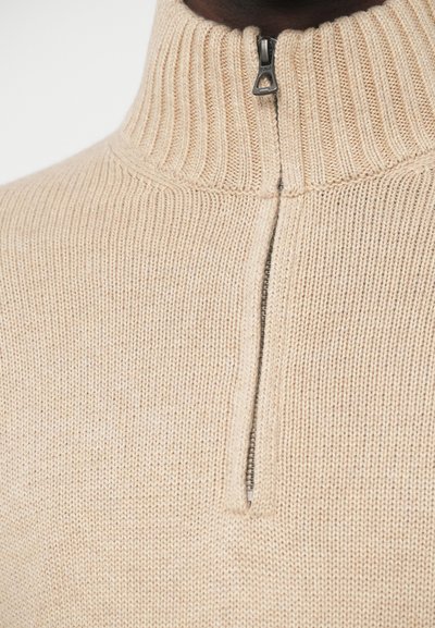 Beige színű, félig cipzáras pulóver texturált kötött anyagból. Bordás nyakkal és fémpullerral ellátott cipzárral rendelkezik. Szoros szabású dizájn.