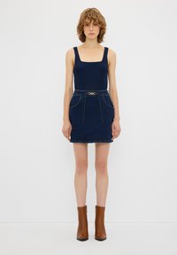 Tumma sininen hihaton bodysuits yhdistettynä farkkuiseen mini-hameeseen, jossa on sivutaskut ja kultaketjun yksityiskohta. Ruskeat nilkkurit täydentävät asukokonaisuuden.