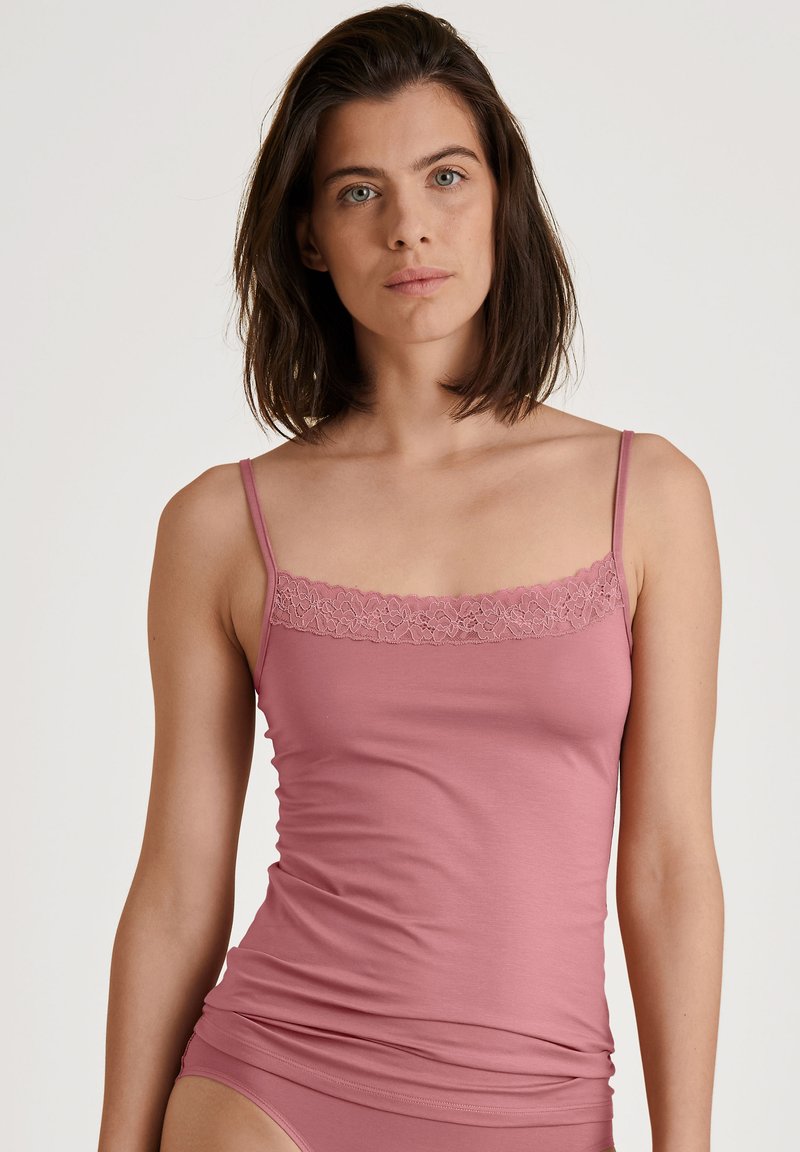 Lichtroze hemdje met kantafwerking bij de halslijn, smalle bandjes en een getailleerd ontwerp, gemaakt van zachte, rekbare stof.