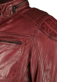 Rote Lederjacke mit hohem Kragen, Reißverschluss-Tasche, strukturierten Schulterakzenten und sichtbaren Steppdetails. Weiche Narbenoberfläche.
