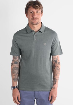 Chemise polo en vert foncé, dotée d'un tissu texturé, d'une patte de boutonnage à trois boutons et d'un petit logo sur la poitrine gauche. Manches courtes.