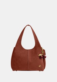 Sac à main en daim marron avec une large anse, logo doré et breloque attachée en forme de cerise dorée et rouge sur fond clair.