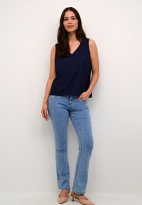 Top fără mâneci de culoare bleumarin cu decolteu în formă de V, asortat cu blugi drepti de culoare bleumarin deschis și pantofi cu toc în nuanța pielii. Look simplu și casual.